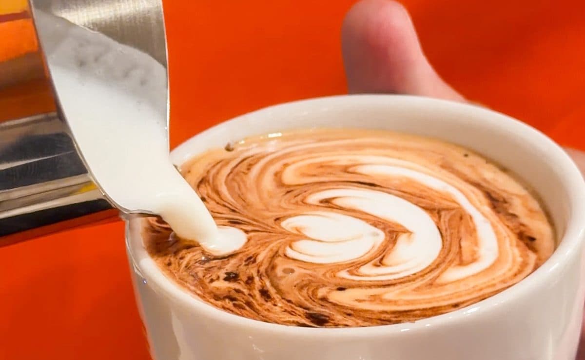 Leite sendo despejado num latte com desenho, na xícara da Mille Cuca